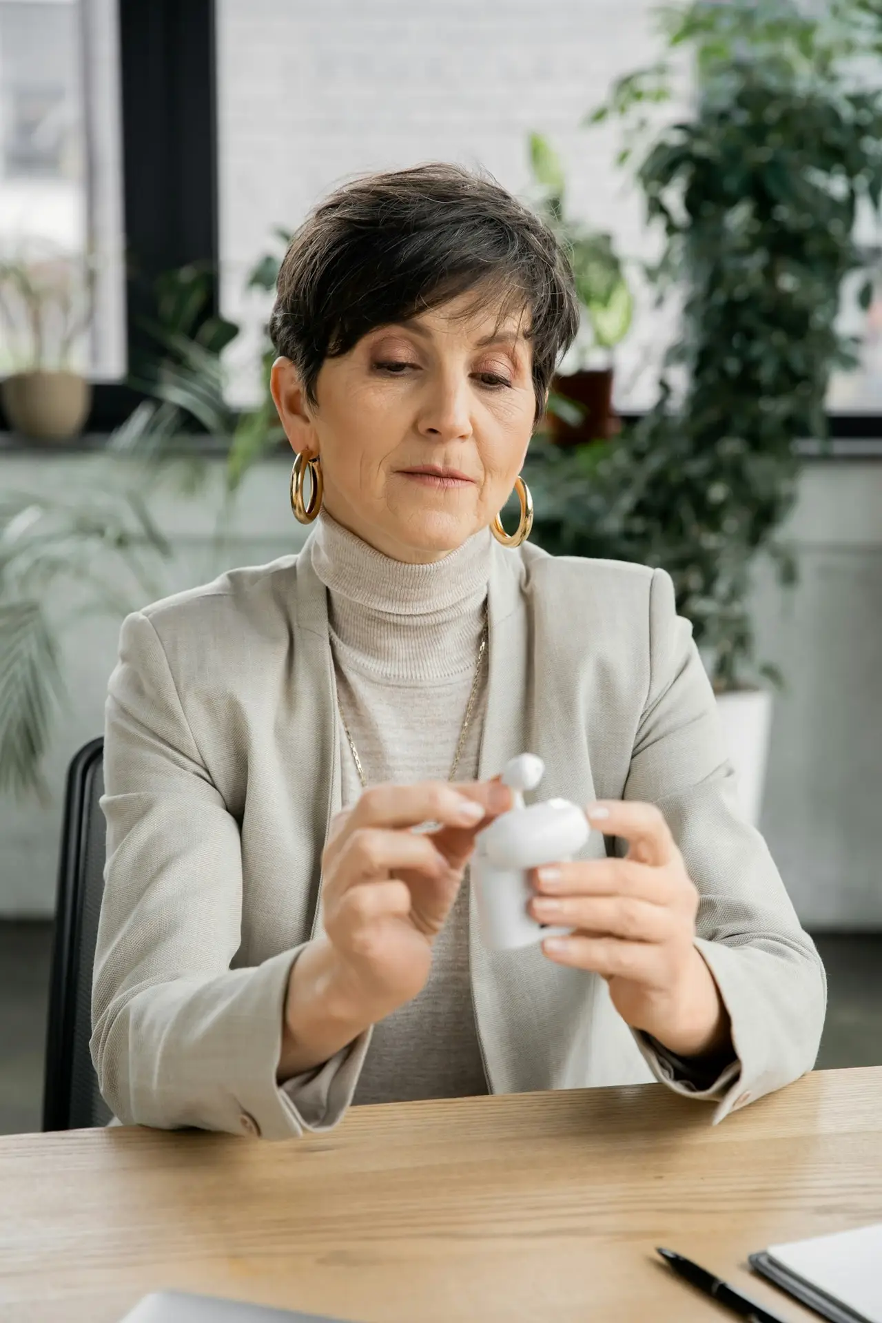 middle aged businesswoman holding earphone case with earbuds at workplace in modern office