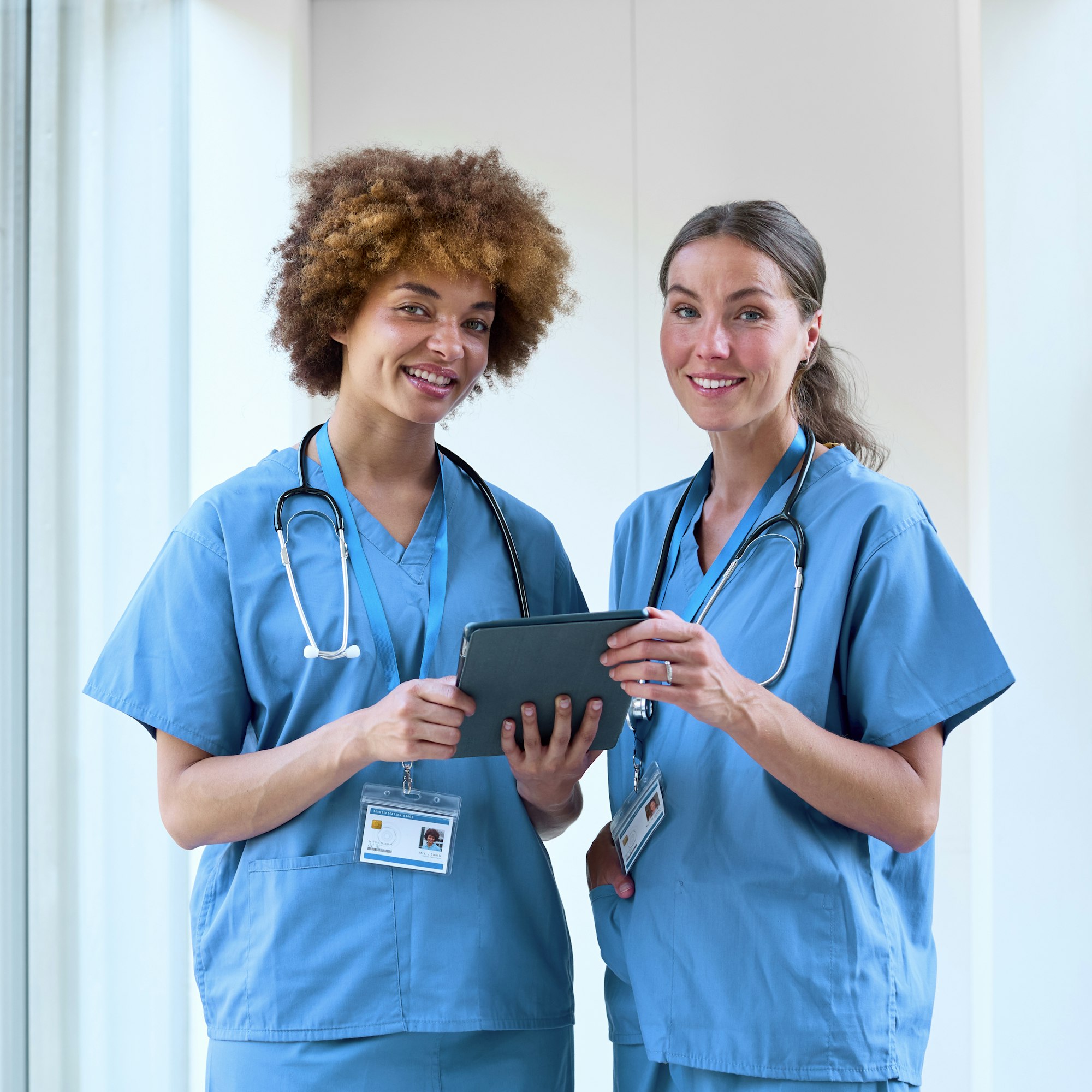 Portrait Of Two Female Doctors Wearing Scrubs With Digital Tablet In Hospital