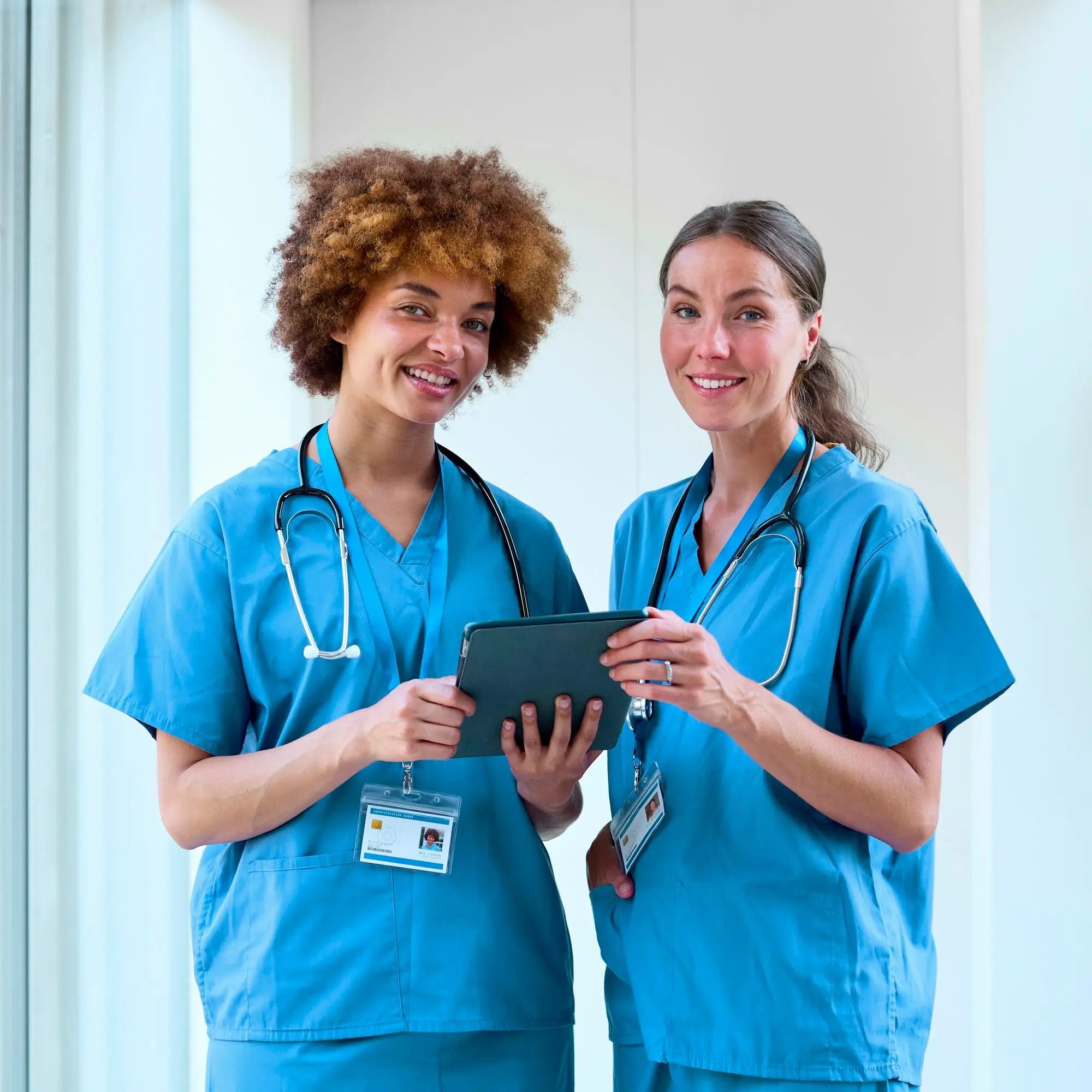 Portrait Of Two Female Doctors Wearing Scrubs With Digital Tablet In Hospital